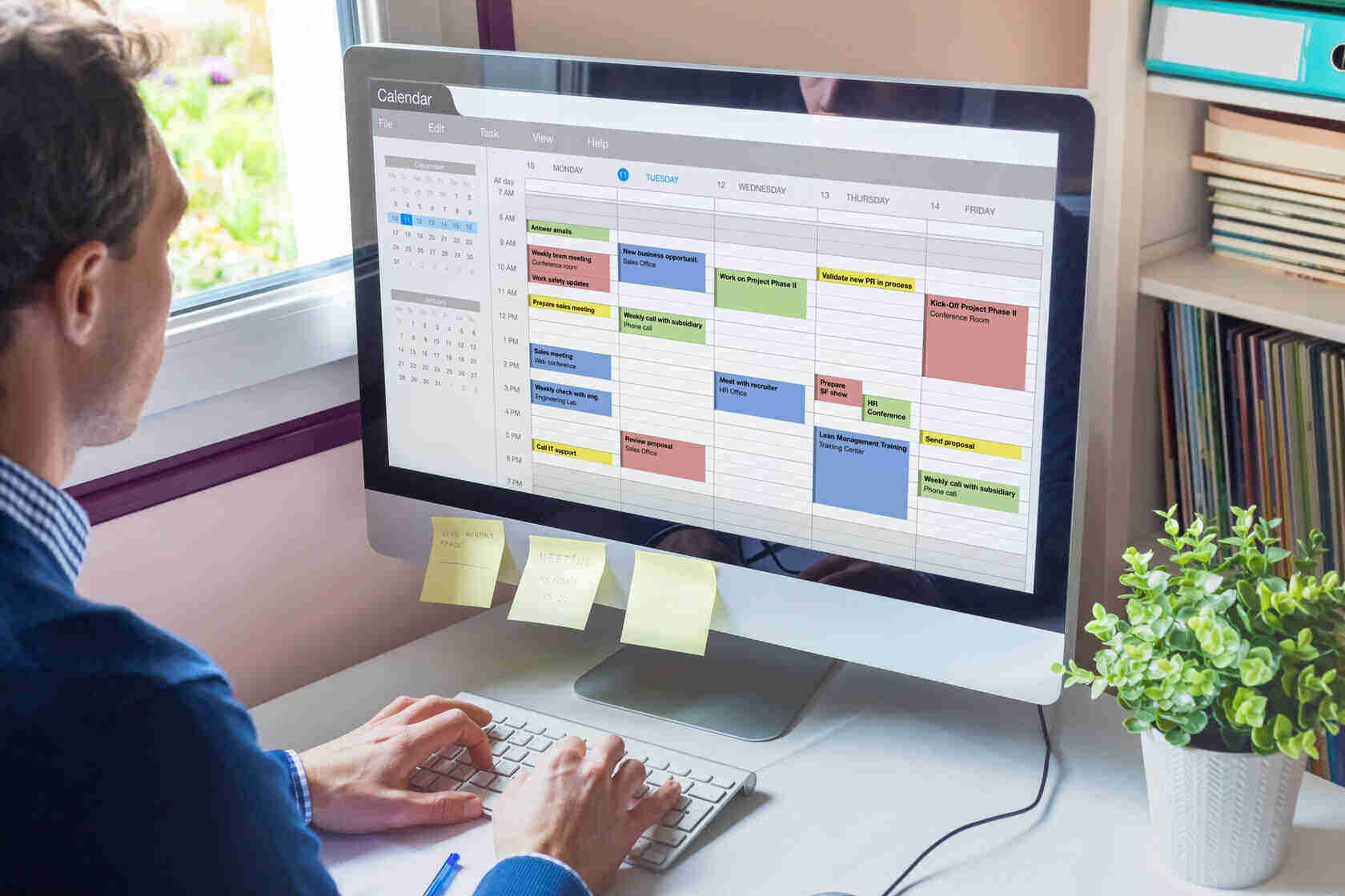 A man uses an imac for calendar management, post it notes, organisation