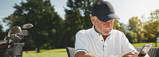 Man looks at smartphone sitting outside at golf course, golf clubs