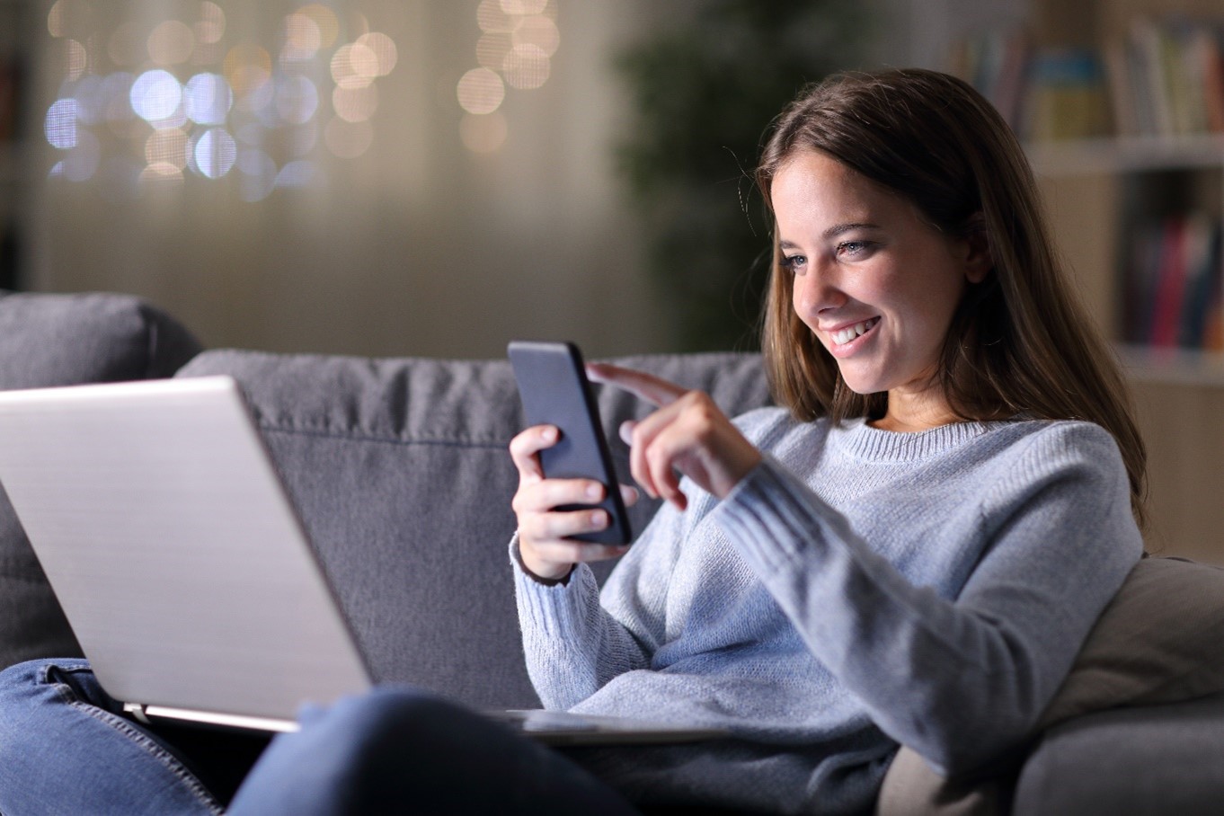 Woman smiling, using a mobile phone and laptop.